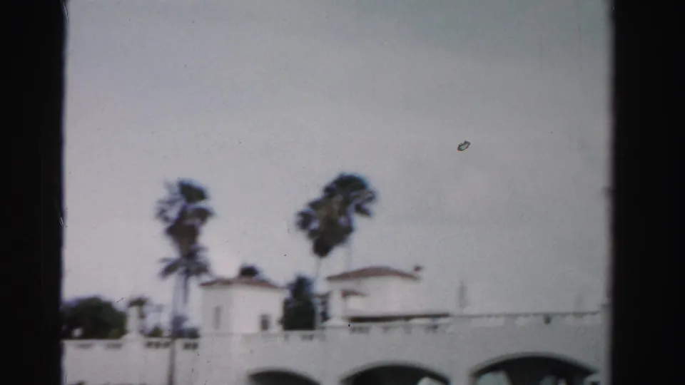 Soft 8mm frame from Dade County in 1955 showing palm trees, a low white bridge wall, and small structures near the water.