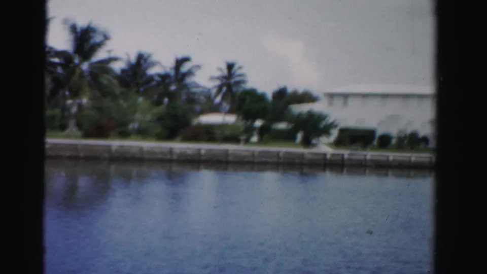 Dade County canal scene with calm water, tropical vegetation, and a low white residential building beyond the bank.