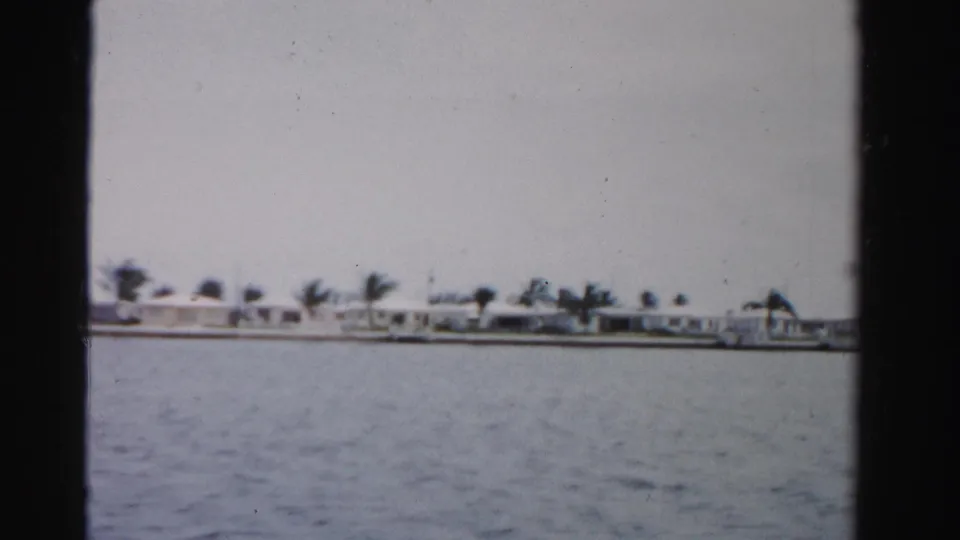 1955 Florida home-movie frame with open water in front of a palm-lined residential shore.