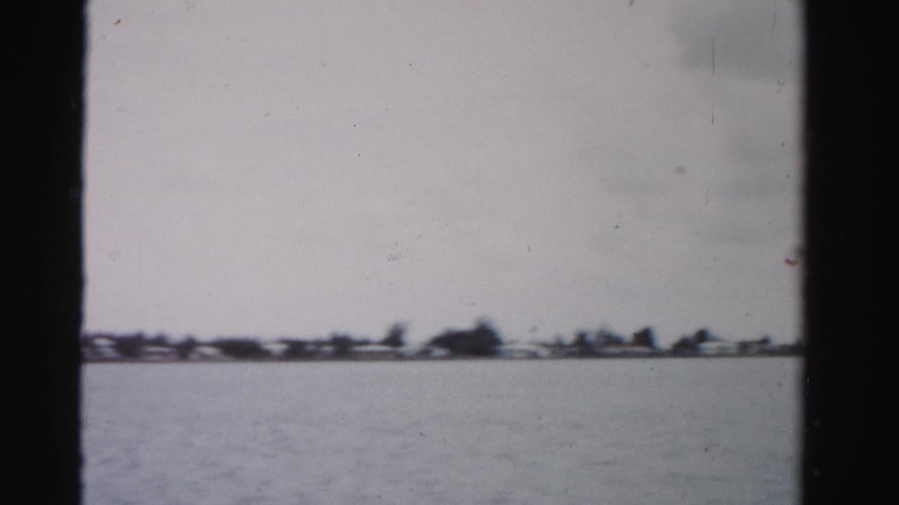 Distant shoreline across open water under a pale sky, framed by dark film edges.