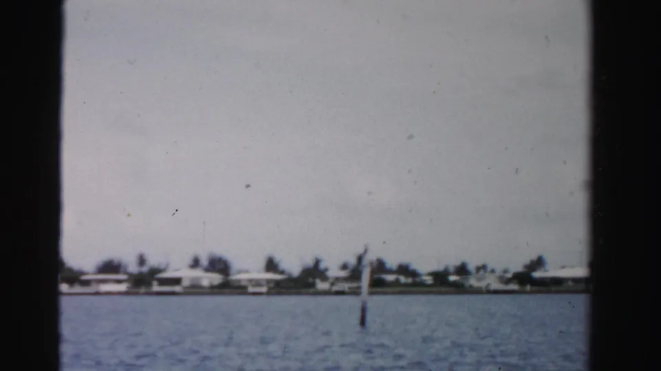 1955 Dade County waterfront frame showing blue-gray water, distant homes, trees, and dark vertical film borders.