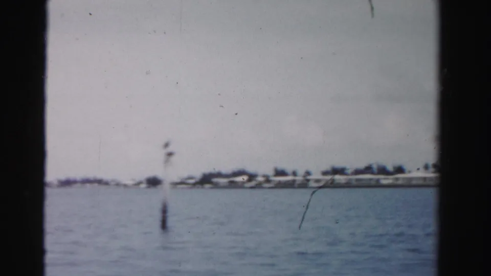1955 Dade County waterway view with a channel post, distant houses, low shoreline, and dark vertical film framing.