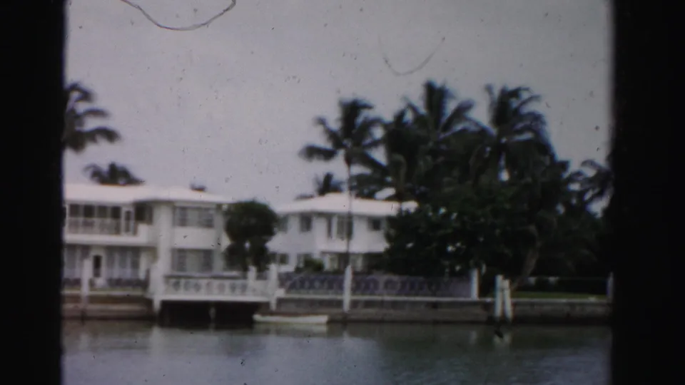 White mid-century waterfront residence with a private dock, palms, and seawall, filmed in Dade County, Florida in 1955.
