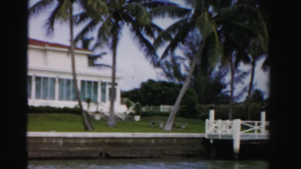 Waterfront lawn and palms in Dade County, with part of a white house and a white dock visible along the seawall.