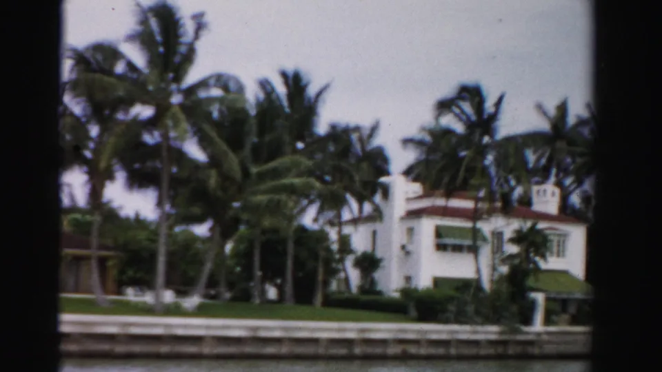Dade County waterfront estate with red-tile roof, tall palms, manicured lawn, seawall, and canal or bay water.
