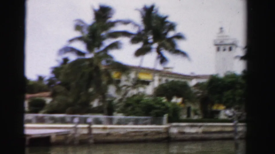 1955 Dade County frame with palms, canal-side structures, railings, seawall, and a distant white tower-like building element.