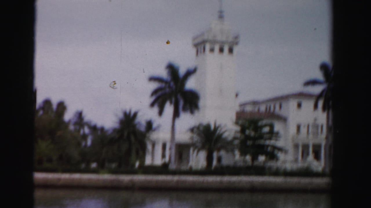 1955 Dade County, Florida 8mm frame of a white Mediterranean-style waterfront estate with palms, viewed from across the water.