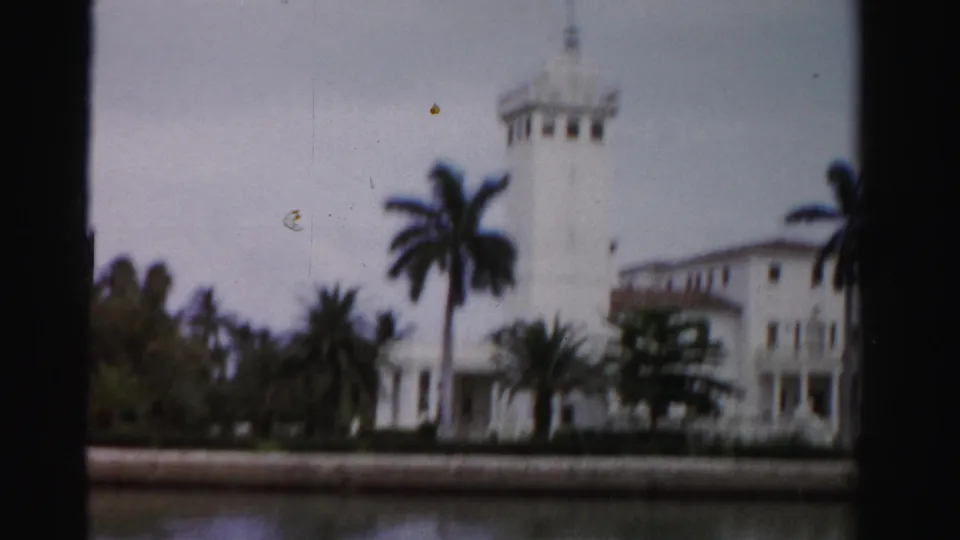 1955 Dade County, Florida 8mm frame of a white Mediterranean-style waterfront estate with palms, viewed from across the water.