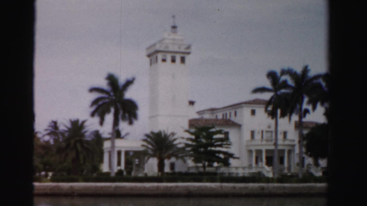 1955 Dade County waterfront view of a white estate with a square tower, balcony, palm trees, and low seawall.