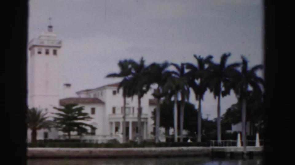 1955 Dade County, Florida frame showing the white waterfront estate behind palms, with a small dock or landing visible at right.