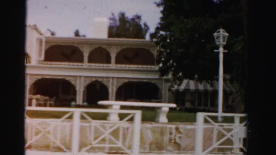 1955 Dade County frame showing the white arched mansion behind rail fencing, with a lamppost, trees, and lawn in view.