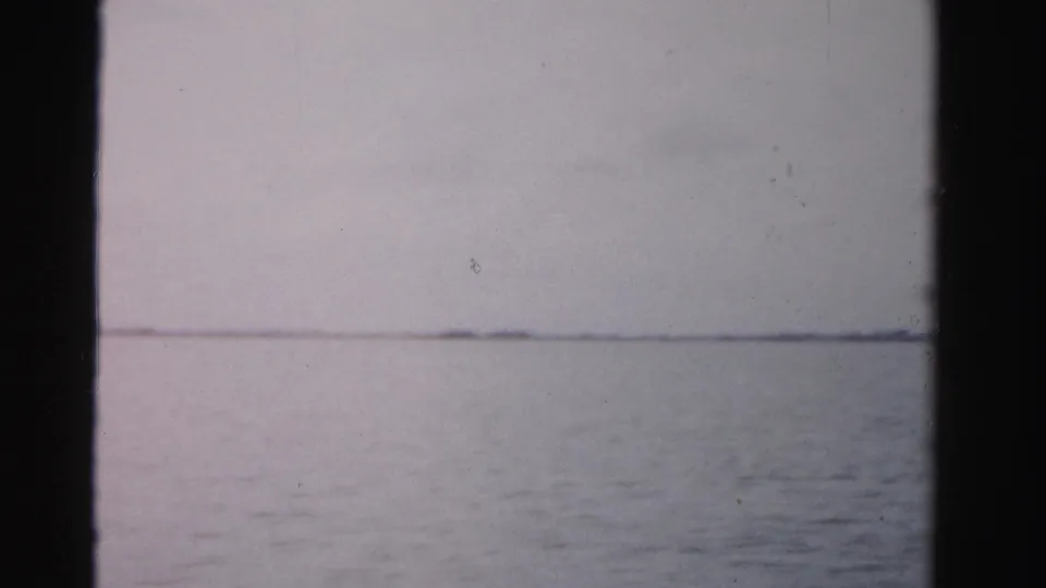 1955 Dade County 8mm frame looking across open water toward a pale horizon, with dark film-edge framing and soft exposure.