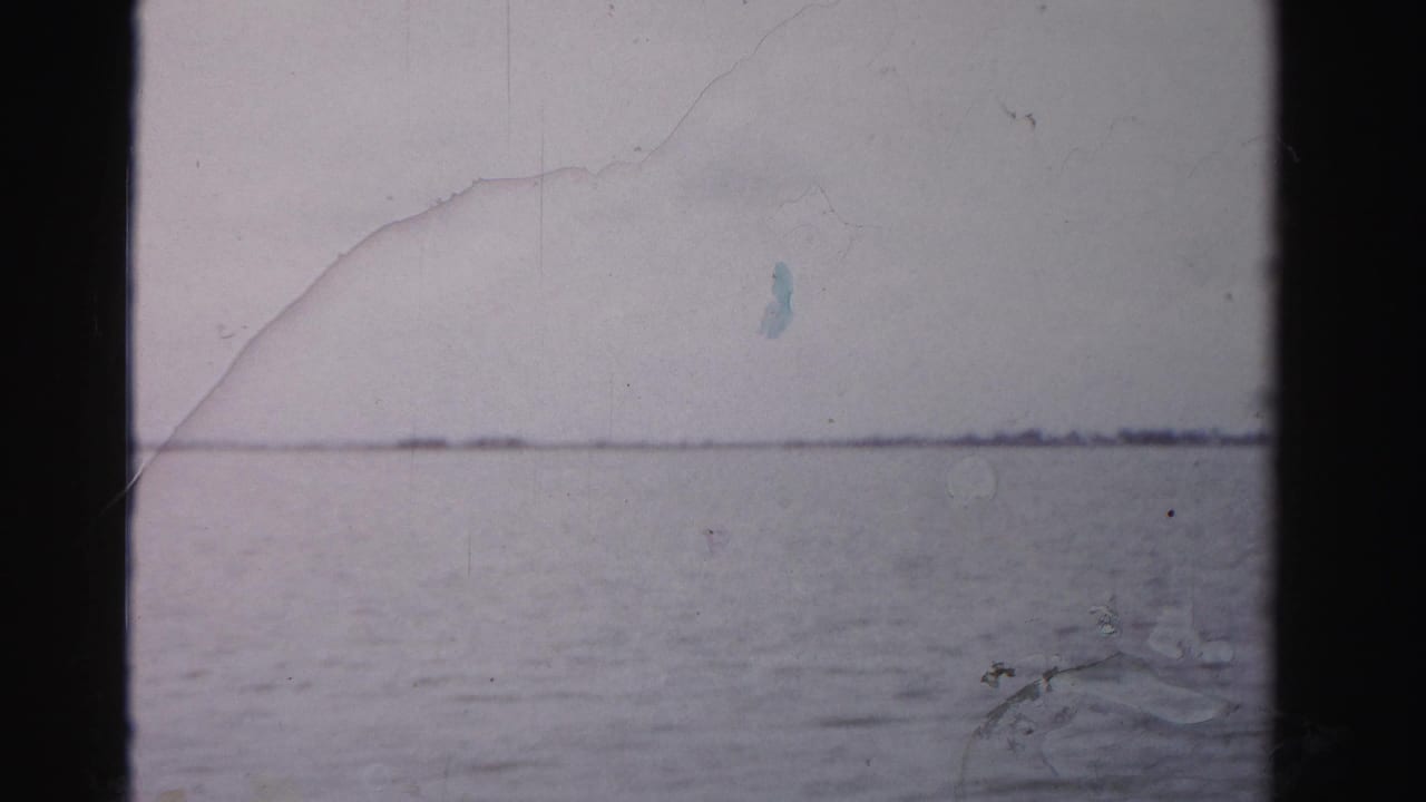 1955 Dade County home-movie frame showing open waterfront under a muted sky before the shoreline building appears.