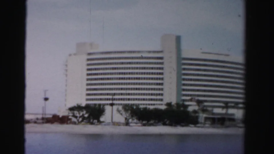 Final frame holds on the white curved waterfront building, shoreline trees, and calm water in Dade County, Florida.