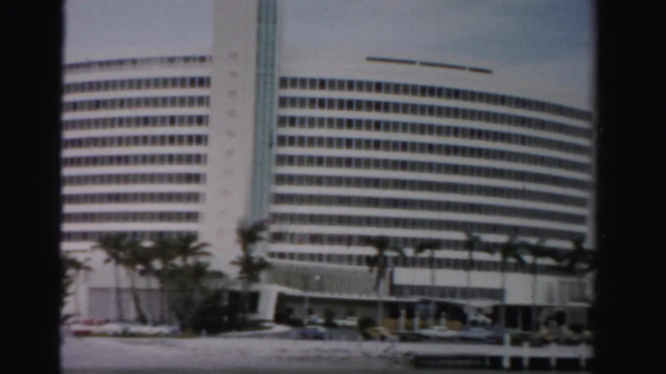 Dade County, Florida, 1955 frame showing the white curved building facade, palm trees, parked cars, and dark film gate edges.