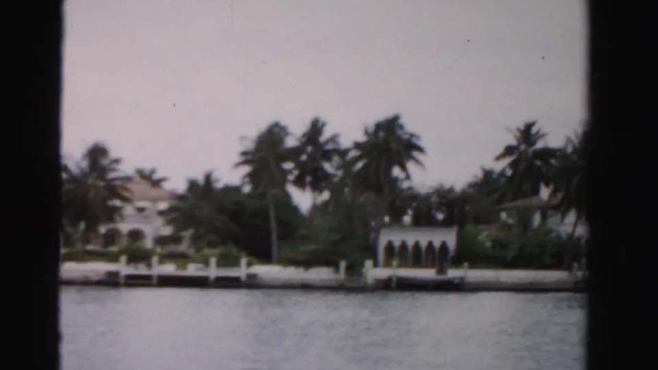 Dade County waterfront estate view from 1955, with palms, white seawall, arched dock area, and homes behind trees.