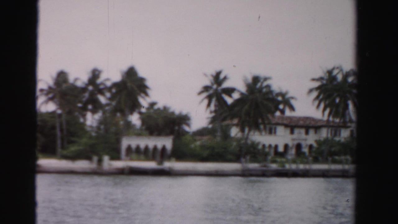 Dade County waterfront residence seen from across the water, with palms and Mediterranean-style arches visible.