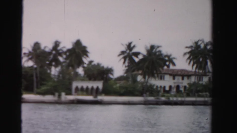 Dade County waterfront residence seen from across the water, with palms and Mediterranean-style arches visible.