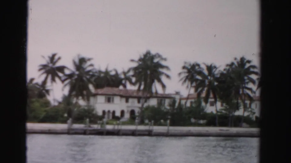 End frame of the 1955 Dade County waterfront view, showing the house, palms, dock edge, and canal or lake water.