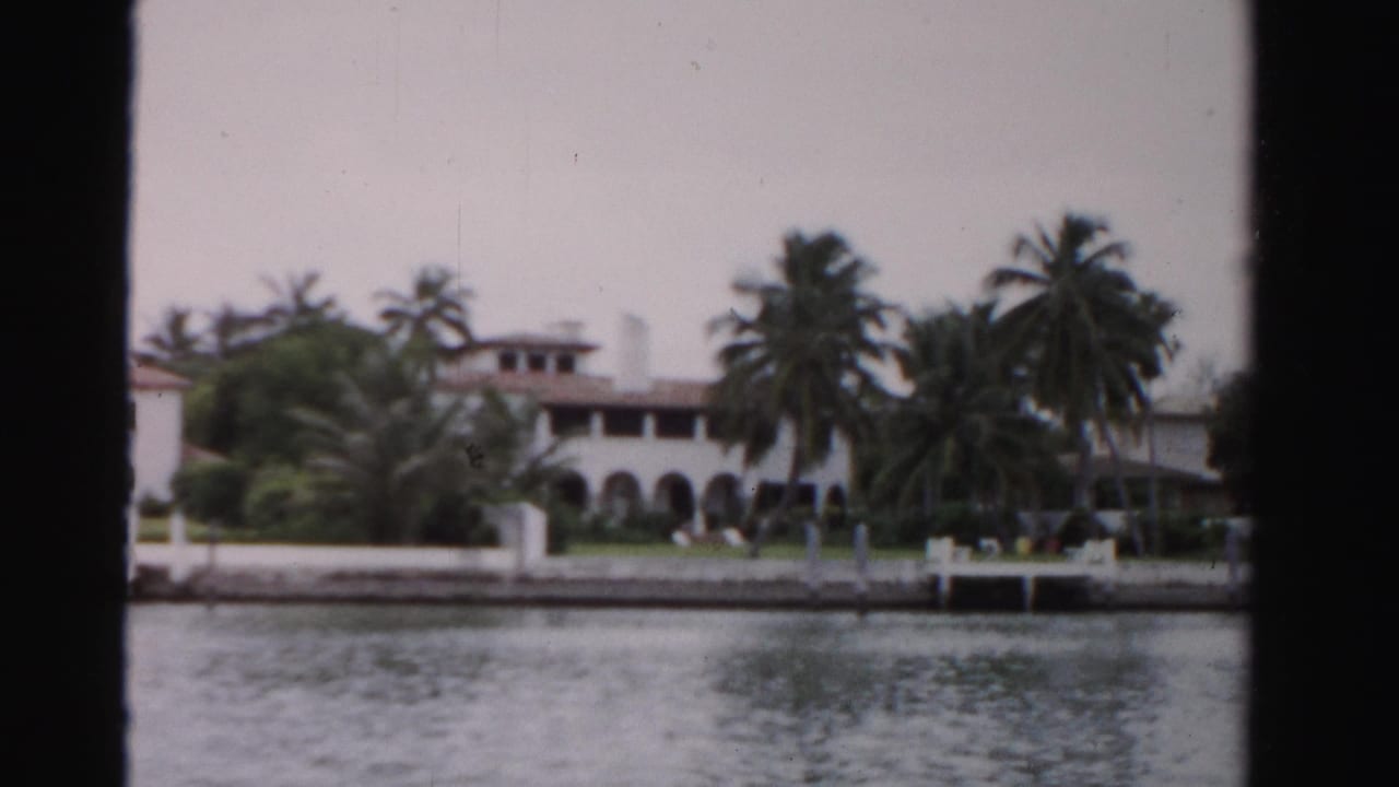 Palm-lined waterfront building with arched openings and dock area.