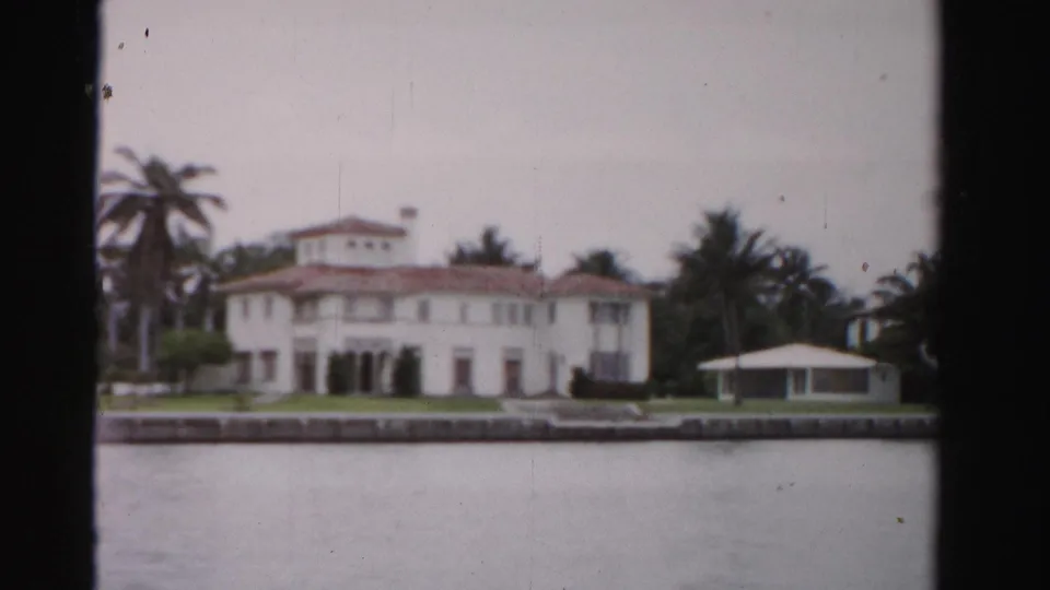 Final 1955 Dade County frame holding on the white Mediterranean-style waterfront mansion, palms, seawall, lawn, and gazebo.