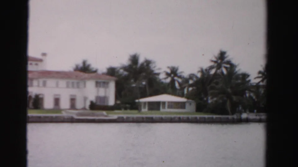 1955 Dade County waterfront property seen in a closer cropped frame, with the mansion partly visible, palms, guest house, seawall, and water.