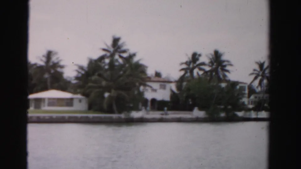 1955 Dade County waterfront estate detail with a small low building, dense palms, seawall, water, and a white house partly visible at right.