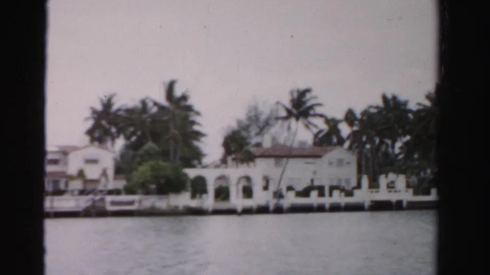1955 Dade County shoreline with white waterfront buildings, arched openings, palms, a seawall, and dock area viewed from across the water.