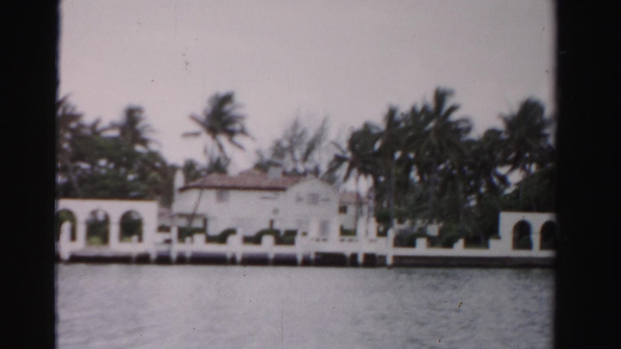 1955 Dade County view of a white waterfront estate framed by palms, with arched loggias along the shore.