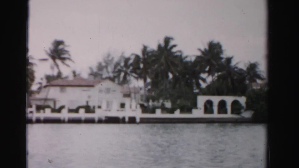 1955 Dade County frame with the waterfront house closer in view, showing white stucco, arches, palms, and water.