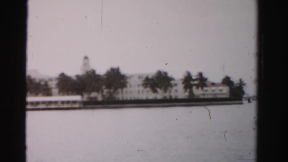 Dade County waterfront view with a long white building, palms, and a tower-like roof feature across the water.