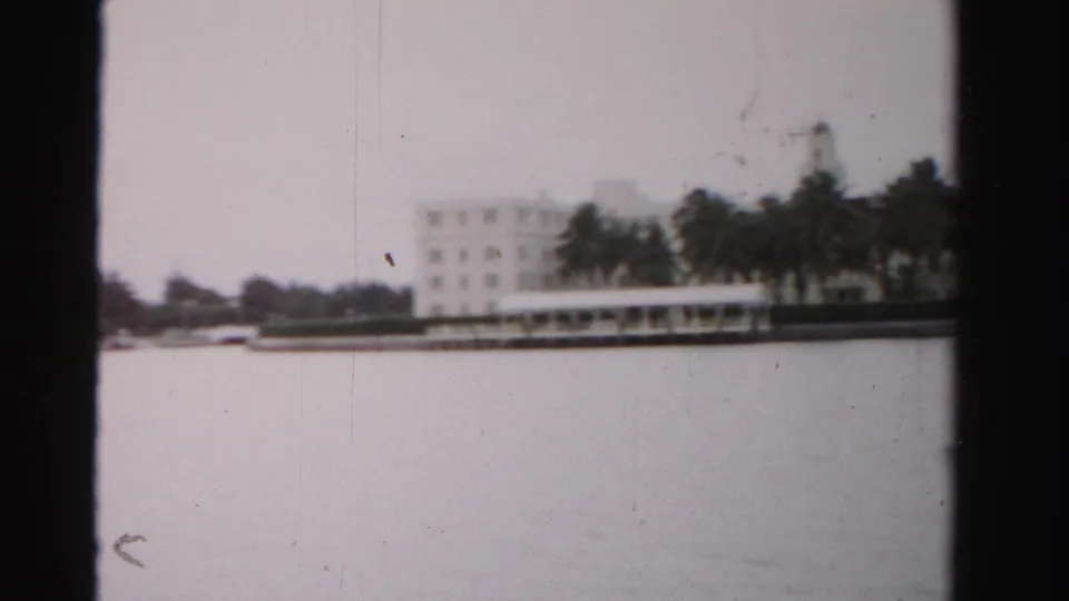 Soft 8mm frame of a Dade County waterfront building partly obscured by palms, viewed from a moving boat or shoreline vantage.