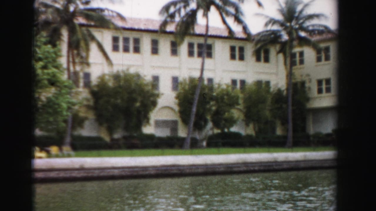 1955 Dade County view from the water of a pale mansion-like building with palms, arched openings, and lawn.
