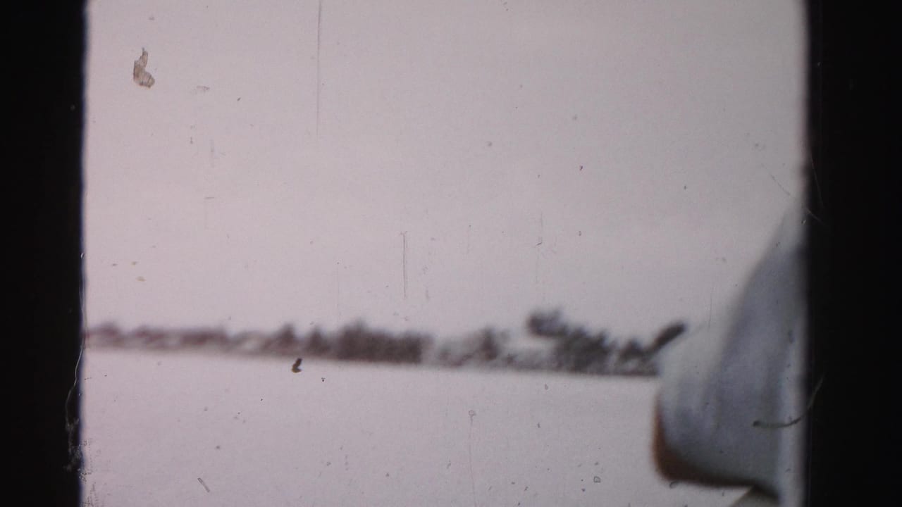 Soft handheld view across water toward a low shoreline, with part of a person or boat edge at right.