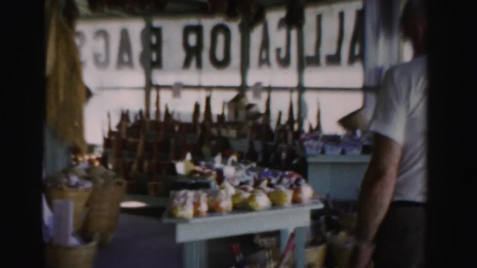 1955 Dade County, Florida 8mm still showing a gift shop interior, souvenir displays, and partial view of a man beside window signage.
