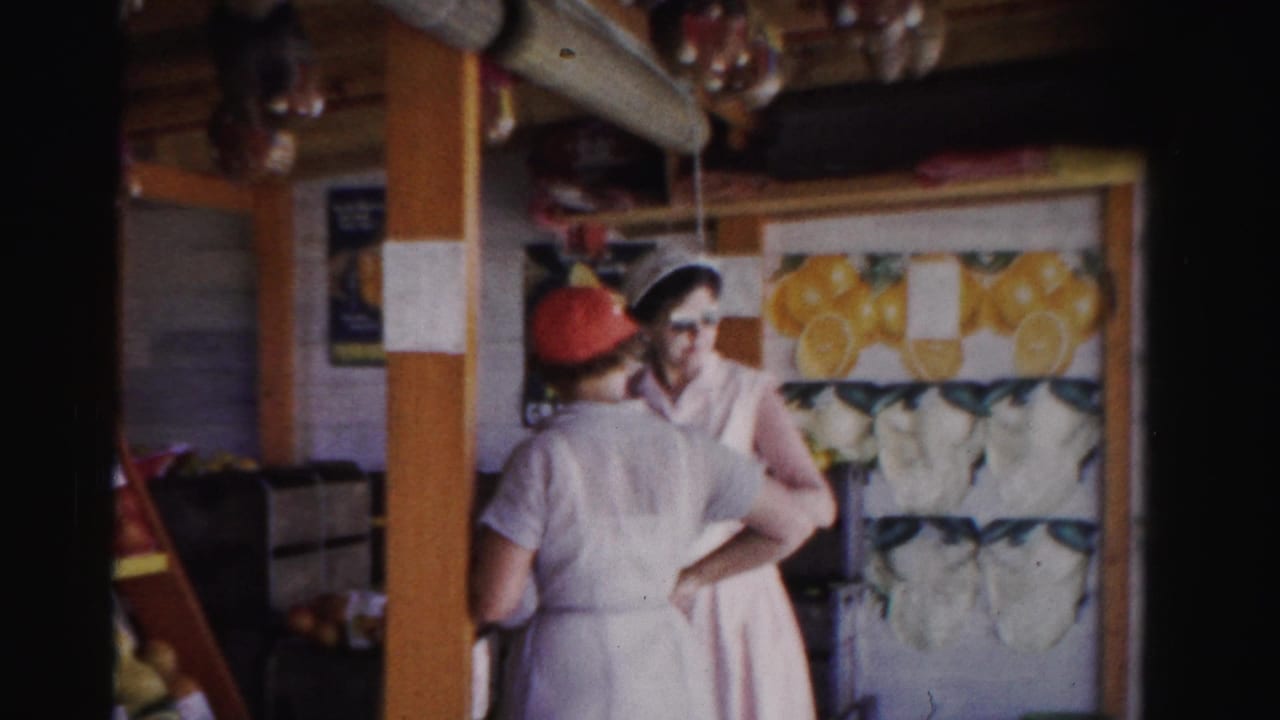 Two women in white uniforms stand behind a fruit stand counter with citrus graphics behind them.