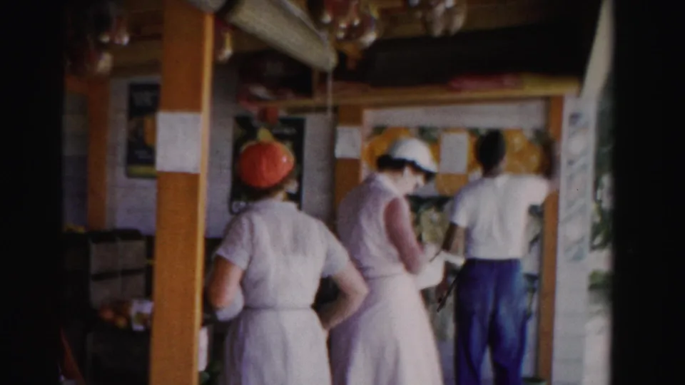 1955 Dade County fruit-stand scene with two women workers and a man entering near crates of produce and citrus signage.