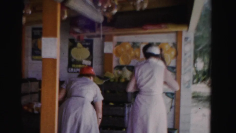 End frame of the 1955 Florida fruit-stand clip showing the women bending or moving near crates under citrus displays.