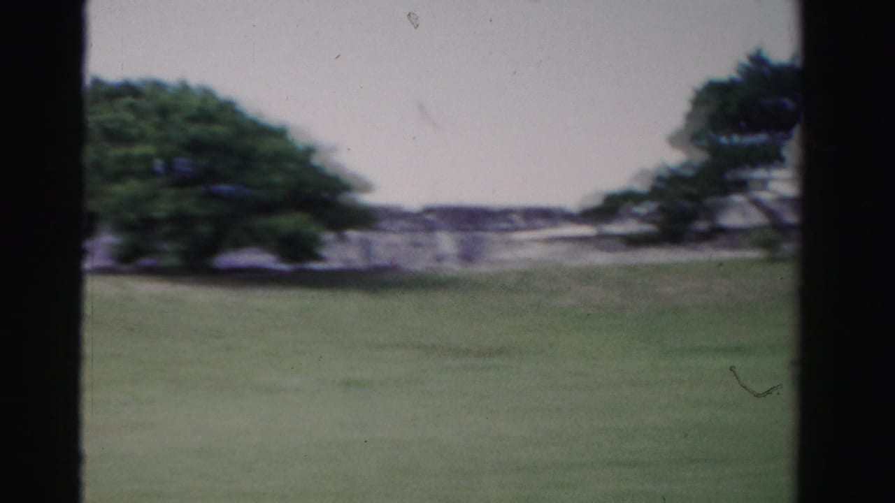 1955 Florida 8mm frame showing a grassy field and distant historic-looking stone wall framed by dark vertical bars.