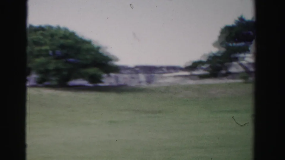 1955 Florida 8mm frame showing a grassy field and distant historic-looking stone wall framed by dark vertical bars.