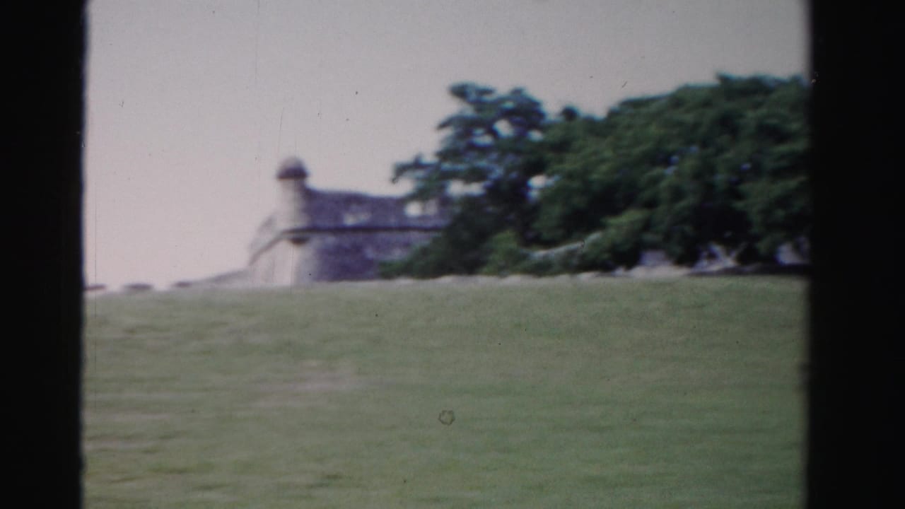 1955 Florida 8mm frame with a distant fort-like masonry structure, flag, open lawn, and trees.