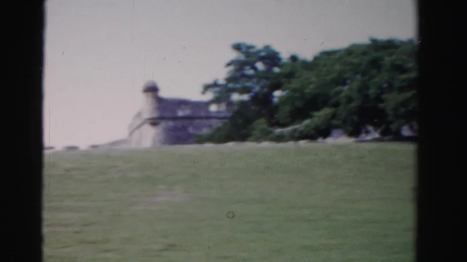 1955 Florida 8mm frame with a distant fort-like masonry structure, flag, open lawn, and trees.