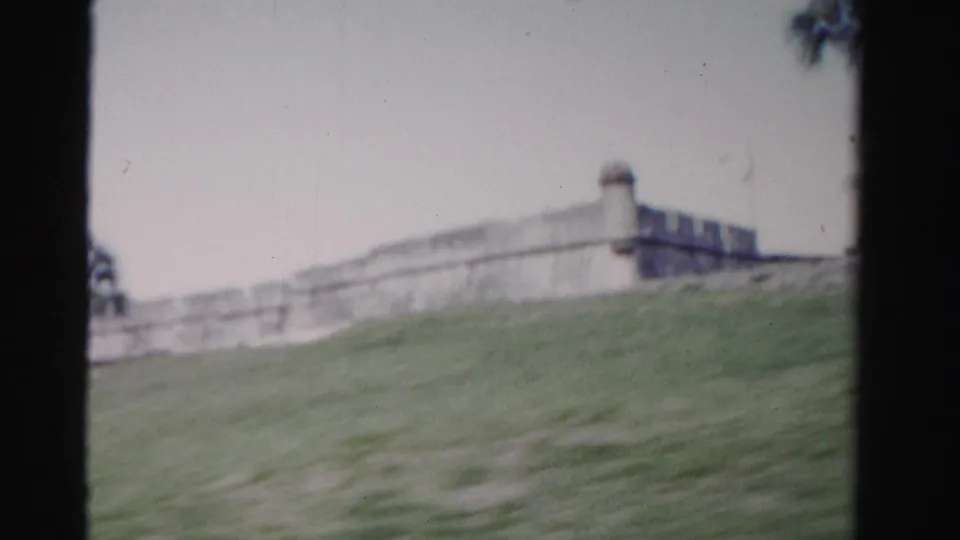1955 Florida 8mm frame showing a sloped lawn leading toward a pale stone wall and fort corner.