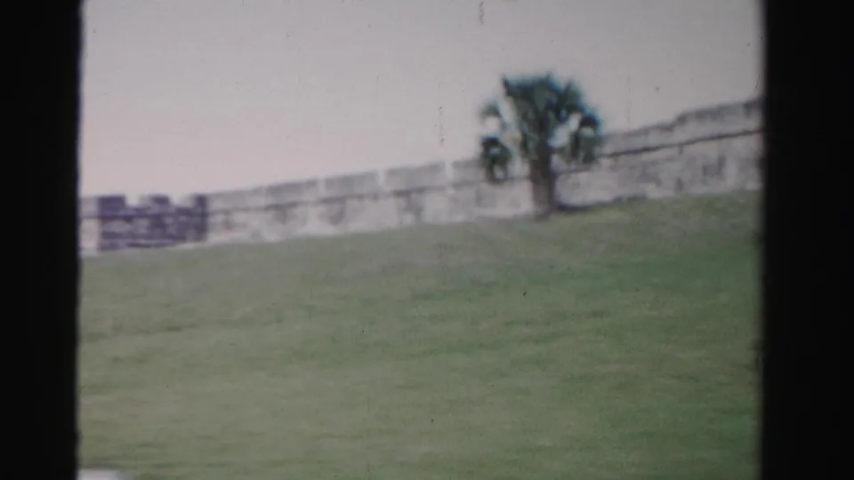 1955 Florida 8mm frame with grassy foreground, pale fort wall, tree, and dark edge framing.