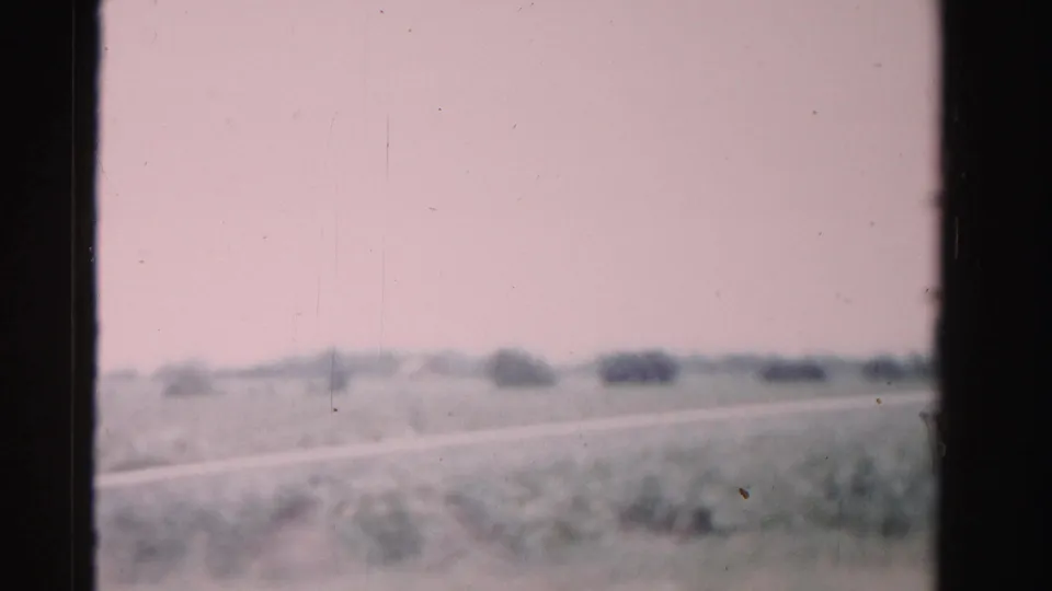 Dade County rail-travel view with soft fields, distant shrubs, a pale horizontal strip, and dark framing from the train window or film gate.