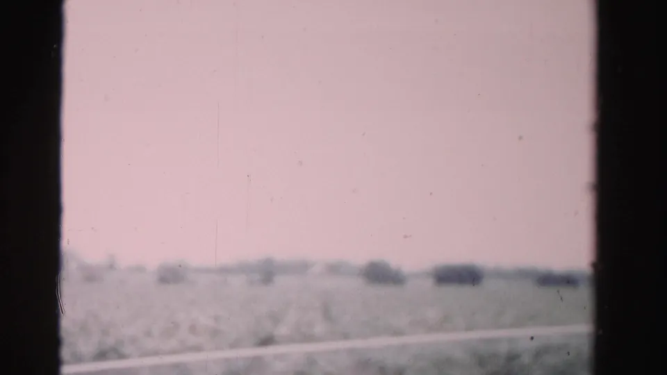 Soft 8mm view from a moving train in Dade County, Florida, showing low fields, distant tree clusters, and heavy dark edge framing.