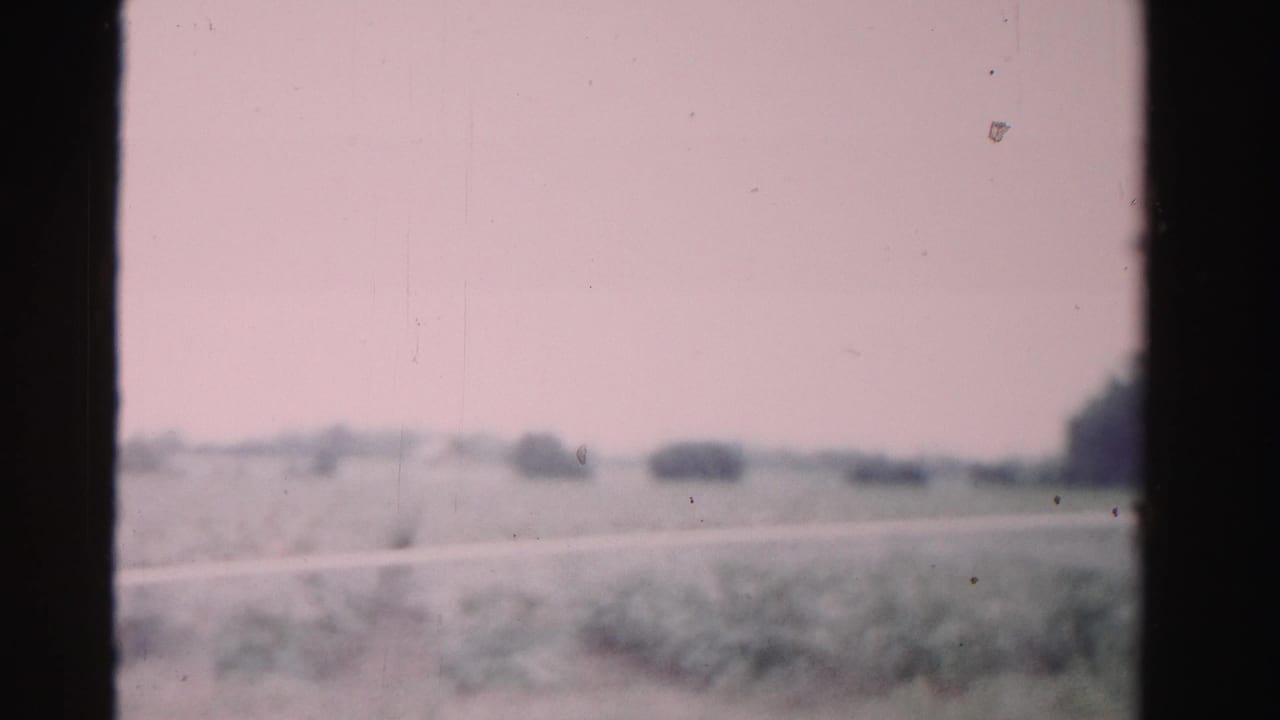 1955 Dade County travel frame with soft-focus fields, distant trees, road edge, and visible 8mm film borders.