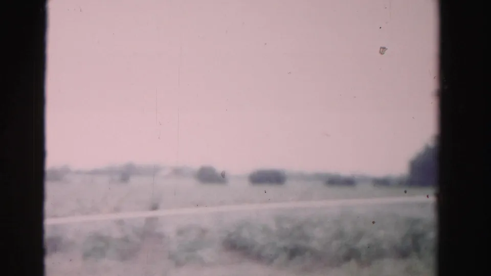 1955 Dade County travel frame with soft-focus fields, distant trees, road edge, and visible 8mm film borders.