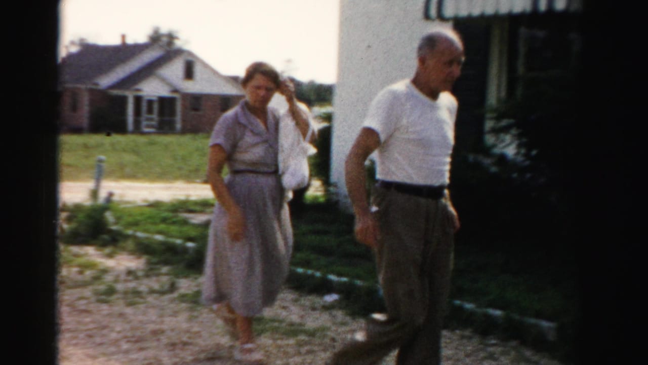Woman in a dress and man in a white T-shirt walking outside a suburban house.