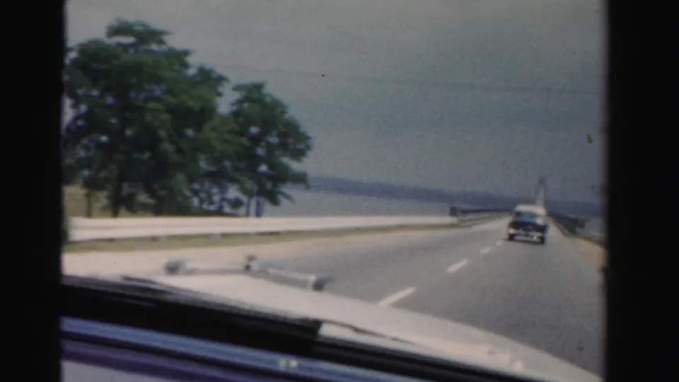 Passenger-view 8mm footage from Dade County, Florida shows the car entering a bridge span with open water and a car ahead.